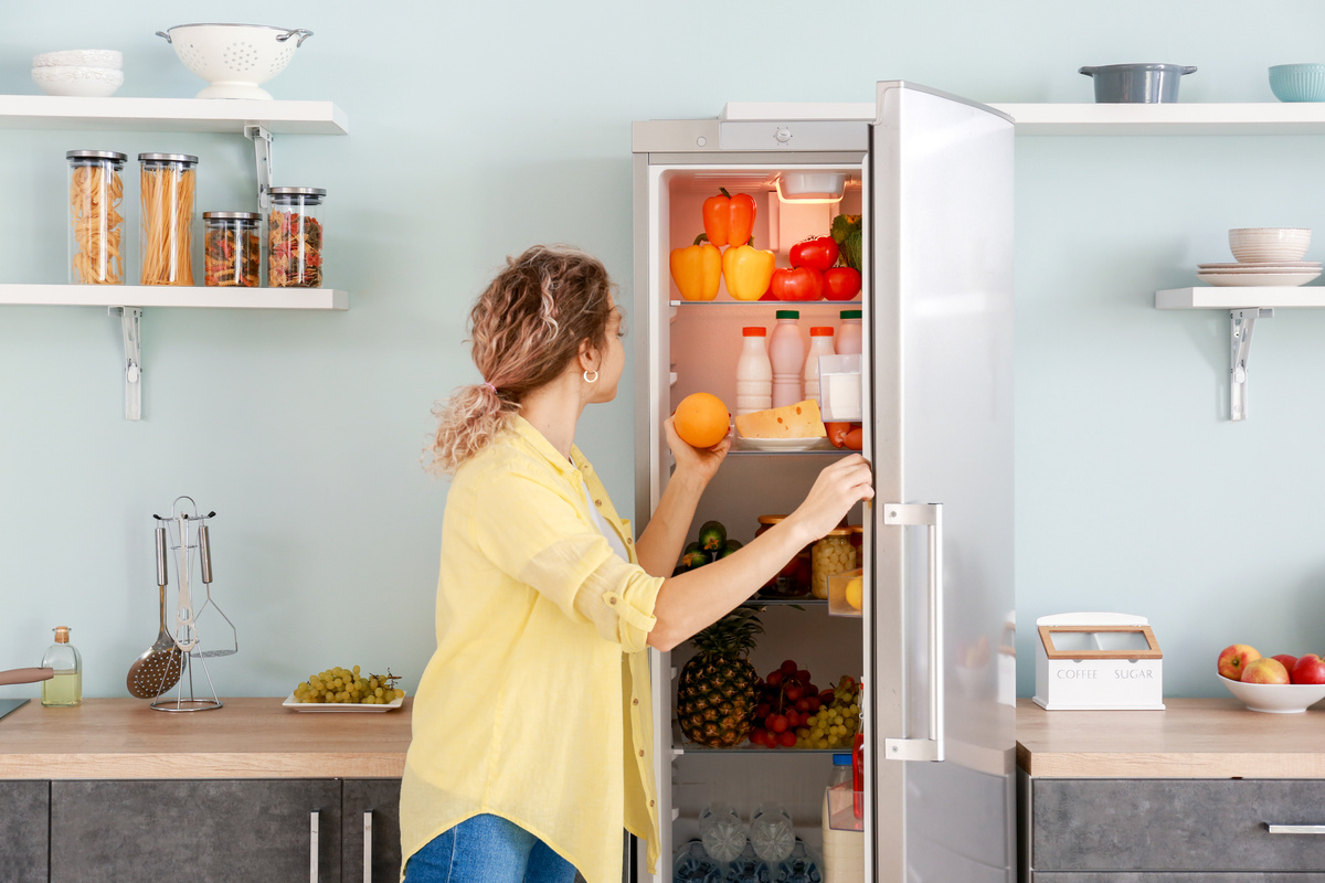 Woman choosing food in modern fridge at home-کاماپرس