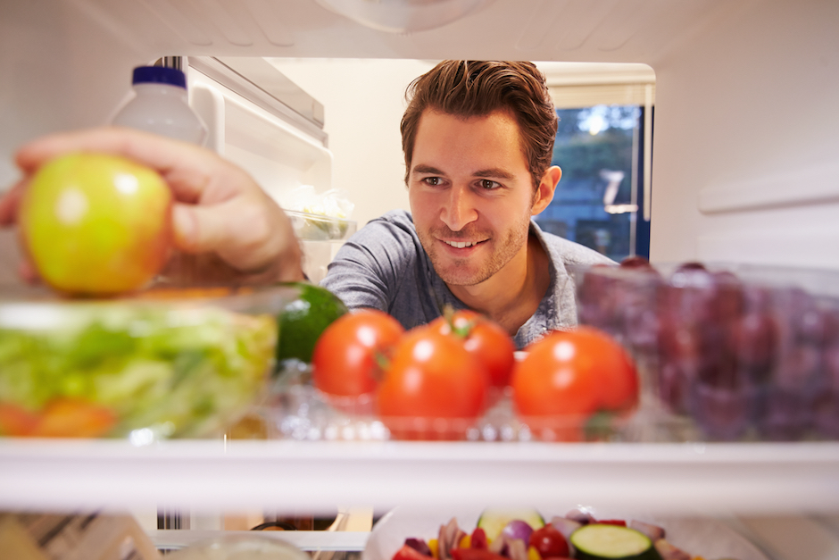 Man Looking Inside Fridge Full Of Food And Choosing Apple