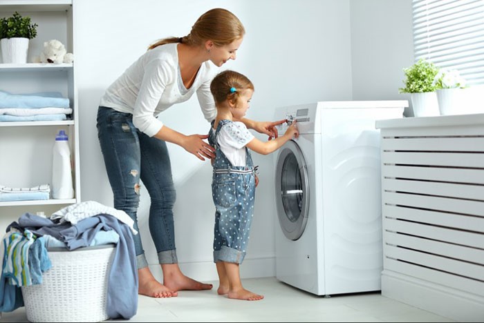 Une personne met des vêtements dans le seau d’une machine à laver-کاماپرس